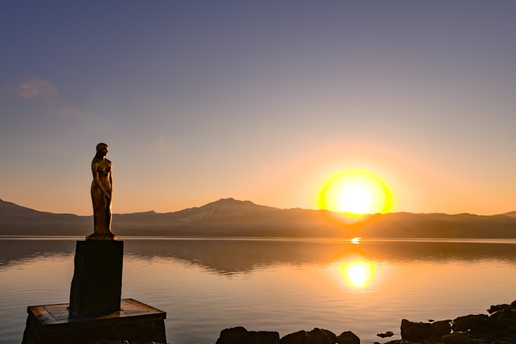 [画像1]田沢湖　辰子姫像と朝陽辰子姫像がシルエットになり今の時期は神秘的な風景を楽しめます。