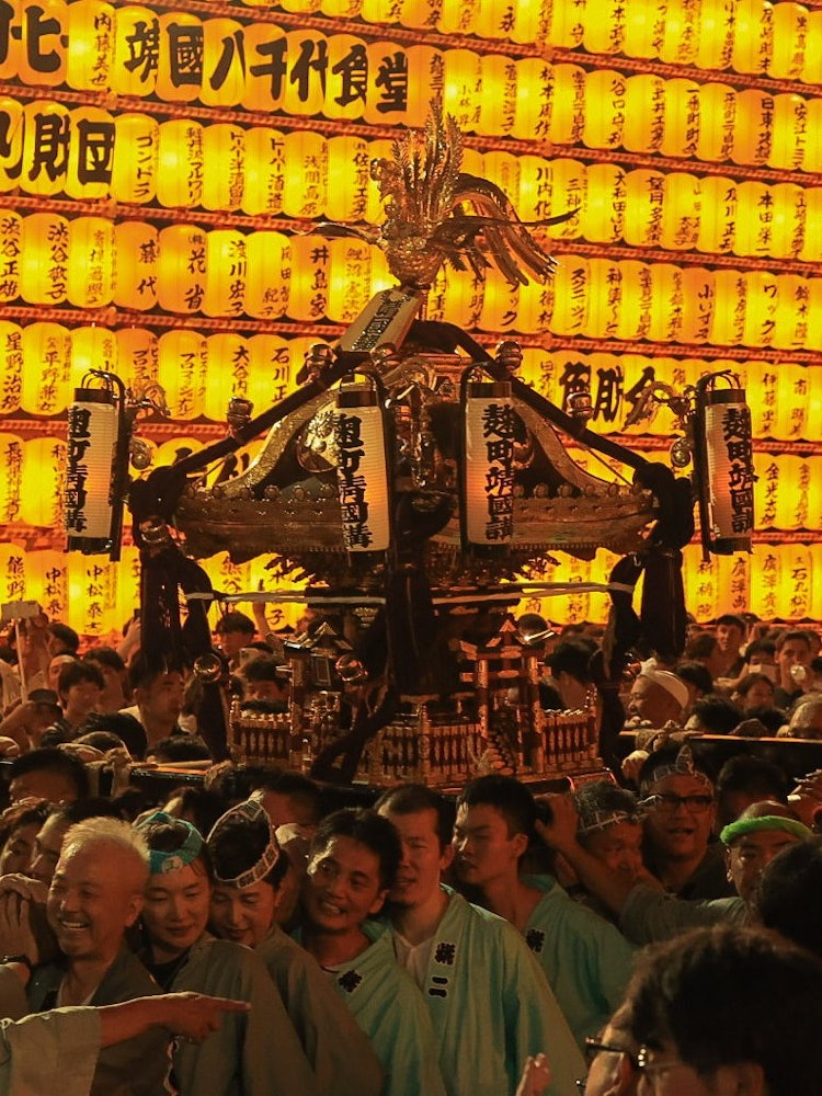 [画像1]東京都千代田区にある靖国神社で開催されたみたままつりを撮影した1枚です。 担ぎ手と神輿が参道の脇にある無数の提灯に照らされて一段と神々しさが引き立てられていました。