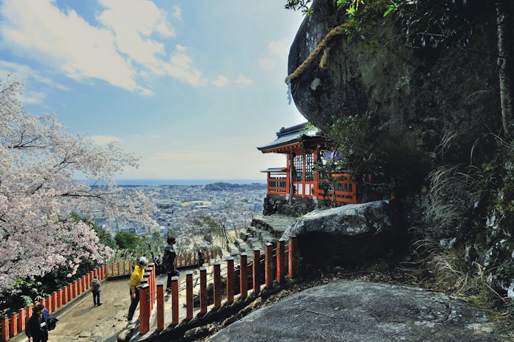 [画像1]和歌山県新宮市の神倉神社です。 ５３８段の急峻な石段の先には、大きな岩・ごとびき岩がご神体として祀られています。 ここからは新宮の街並みが一望できます。 ２月６日には、白装束に身を包み、松明を持った上