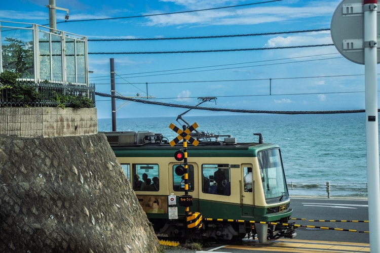 [相片1]江之島電鐵，鐮倉高中前1號鐵路道口，鐮倉高中前站。 它也是某些動漫的聖地，許多遊客參觀了它。 夏天的藍天和大海，是江之電列車砰的一聲駛過的時刻。