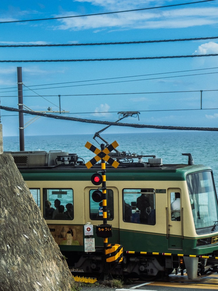 [画像1]江ノ島電鉄、鎌倉高校前駅すぐ近くの鎌倉高校前 1号踏切。 某アニメの聖地となっているのもあり、多くの観光客が訪れていた。 夏の青い空と海、そこに江ノ電の電車がガタンゴトンと通過する瞬間の一枚。